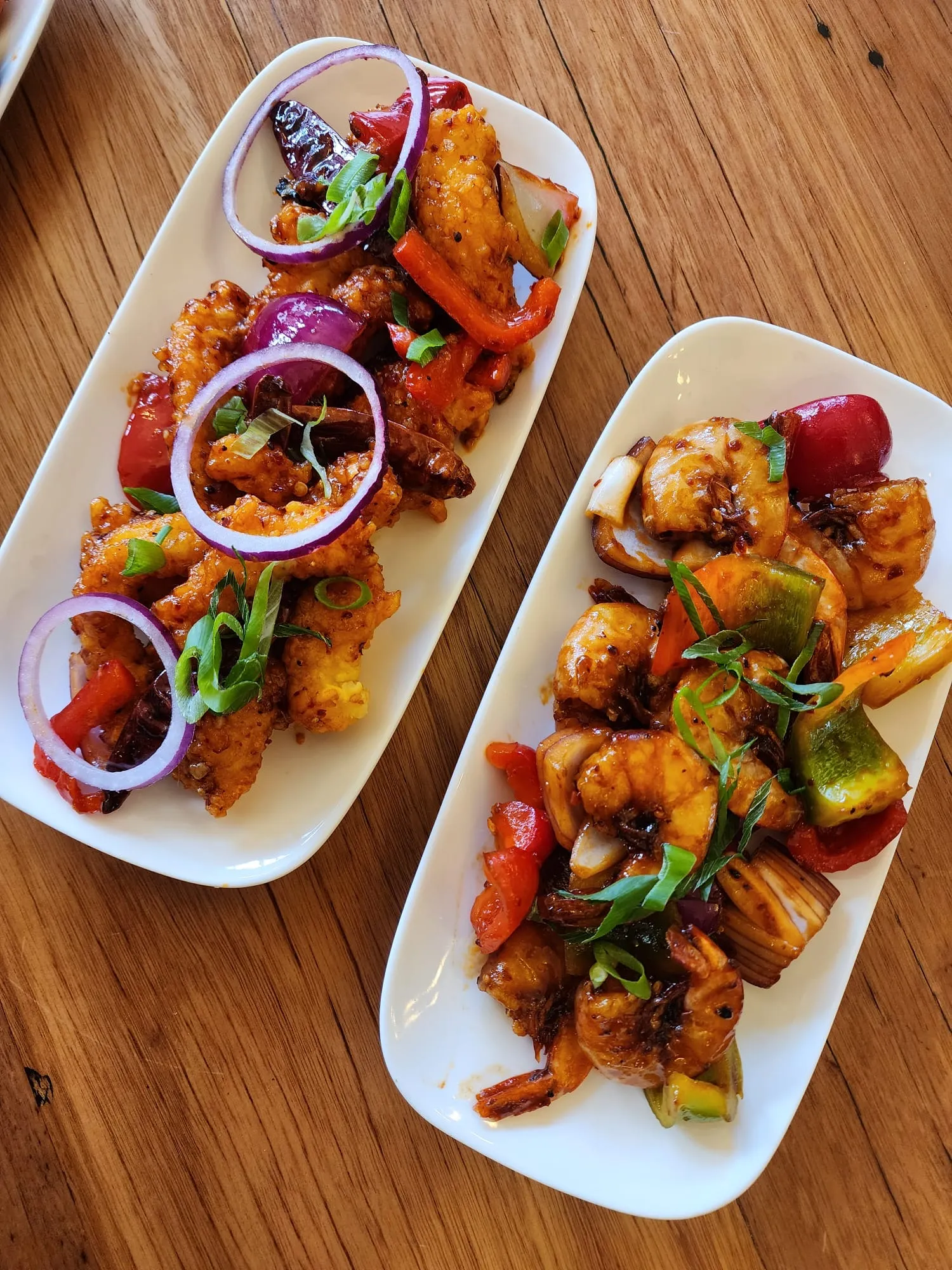 Two plates of devilled cauliflower and devilled prawns with peppers and onion