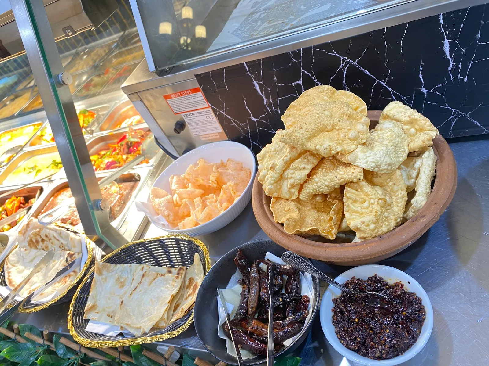 Buffet display of pappadams, flatbreads and Sri Lankan short eats behind glass