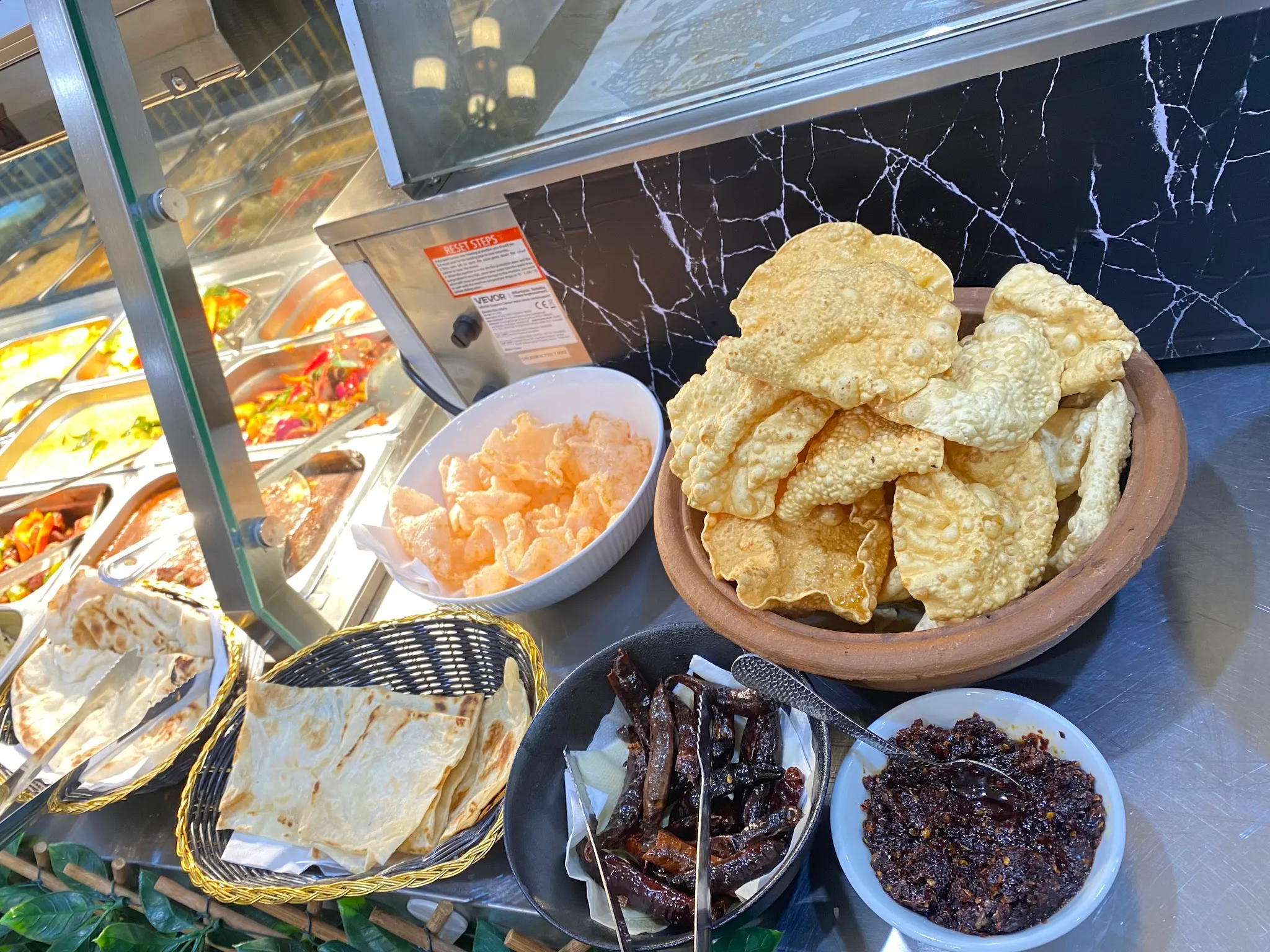 Buffet display of pappadams, flatbreads and Sri Lankan short eats behind glass