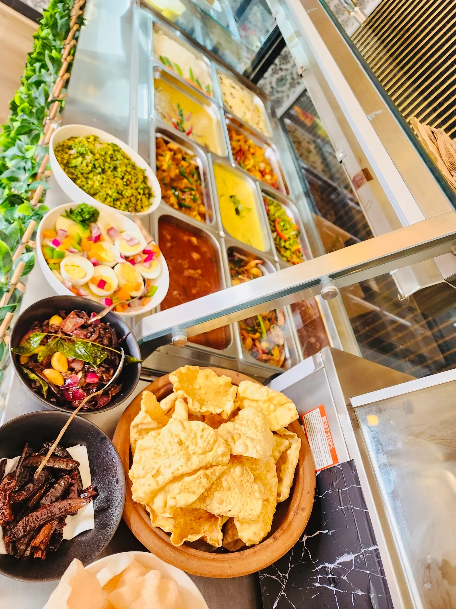 Angled buffet counter with pol sambol, pappadams and curry trays