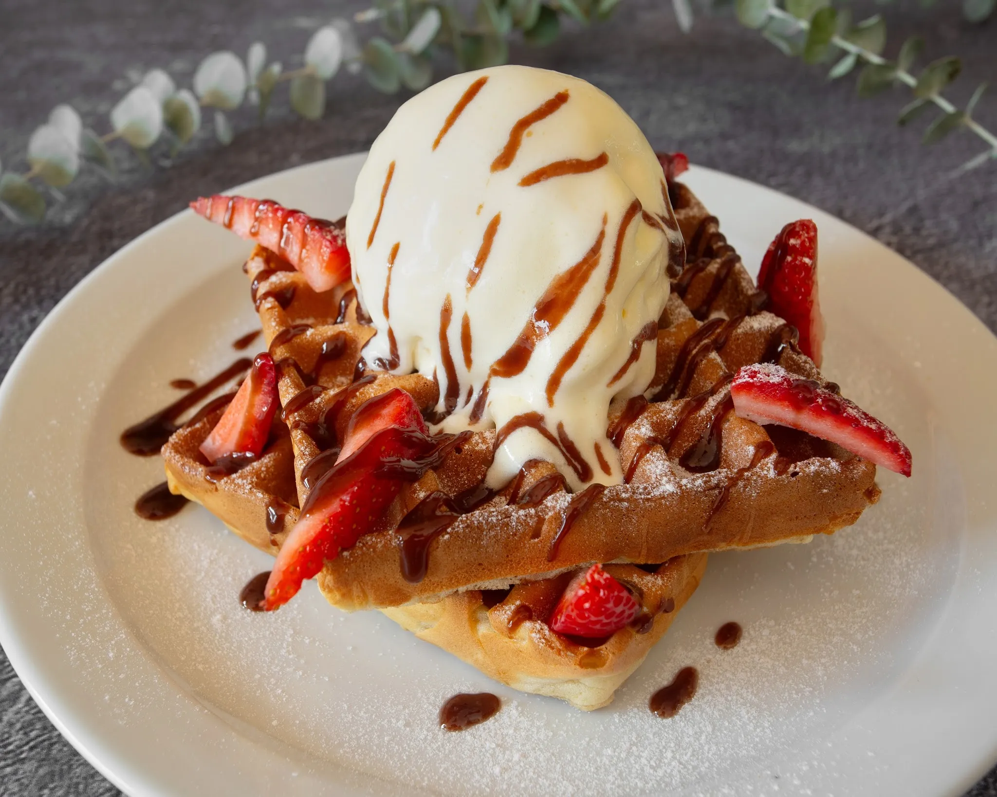 Belgian waffle with ice cream, strawberries and chocolate drizzle on a plate