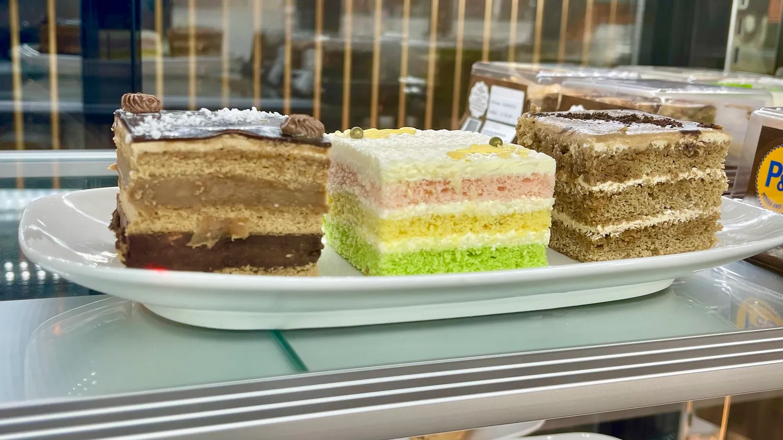 Three slices of layered cake on a platter in a glass display cabinet