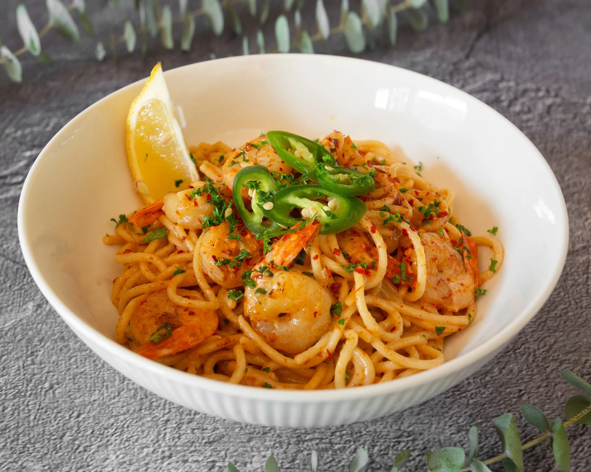 Bowl of seafood noodles with prawns, green chilli and a lemon wedge