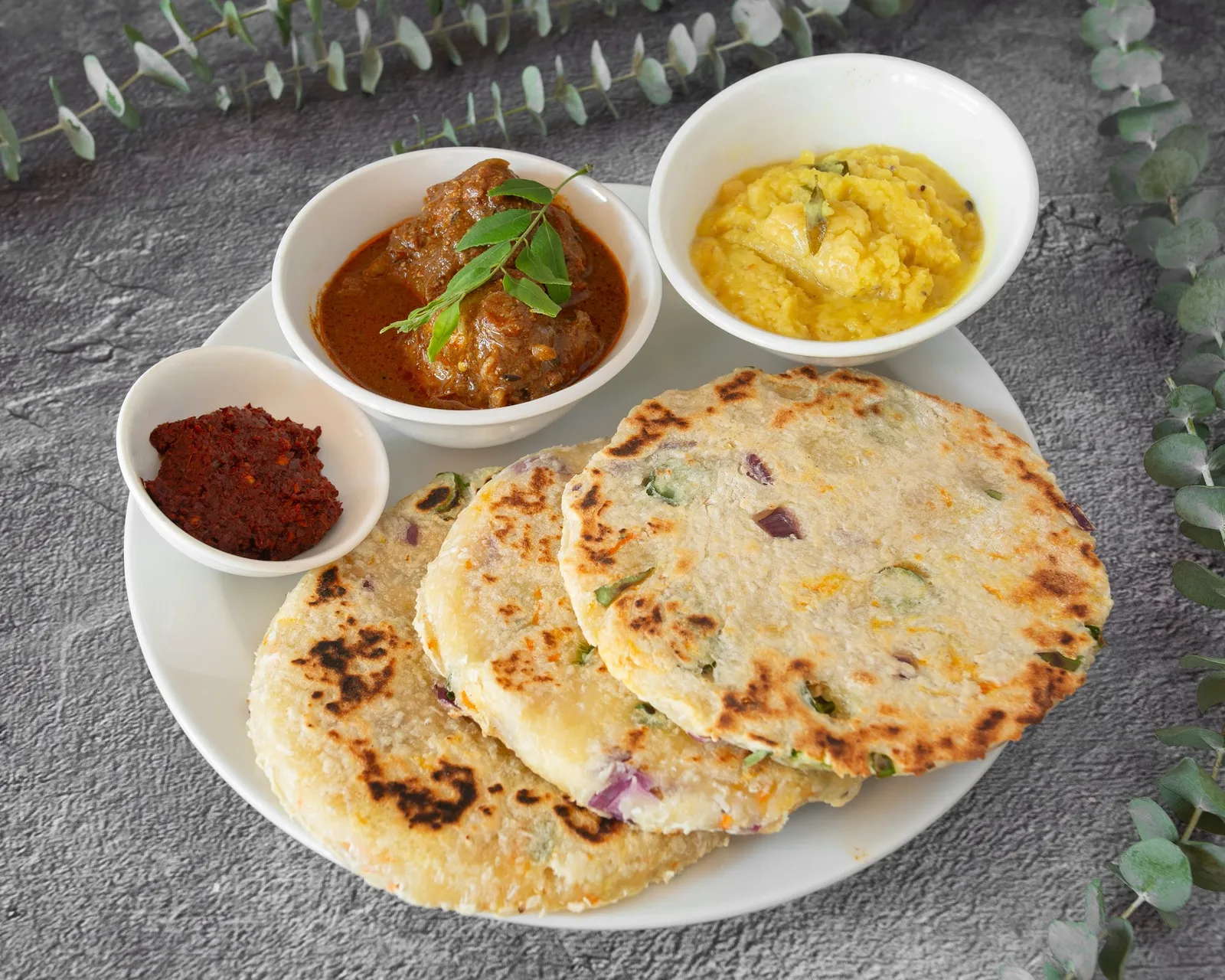 Coconut roti with meat curry, dhal and chilli sambol on a white plate